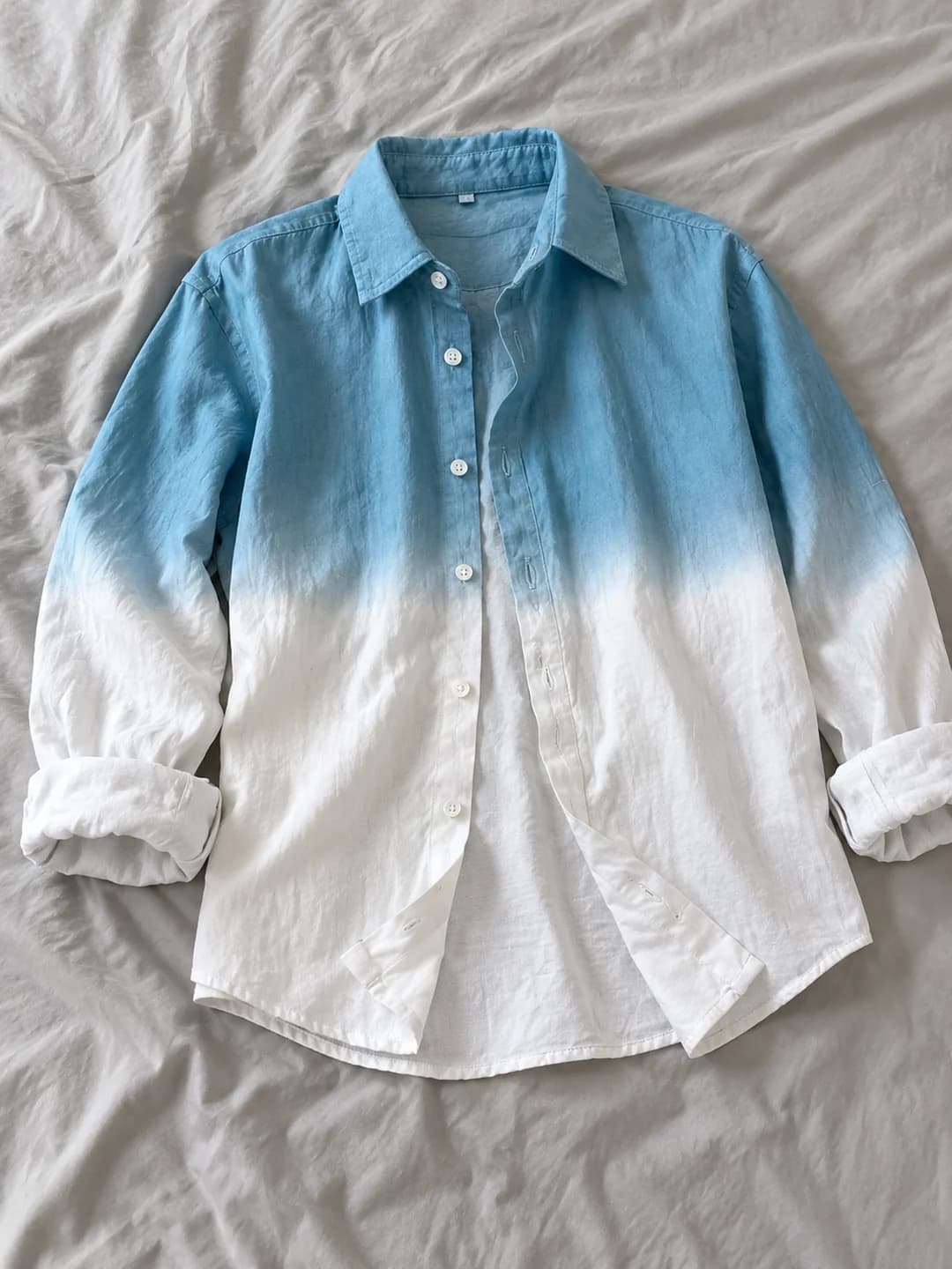 Supplied photograph of a blue-to-white ombré shirt laid on pale fabric